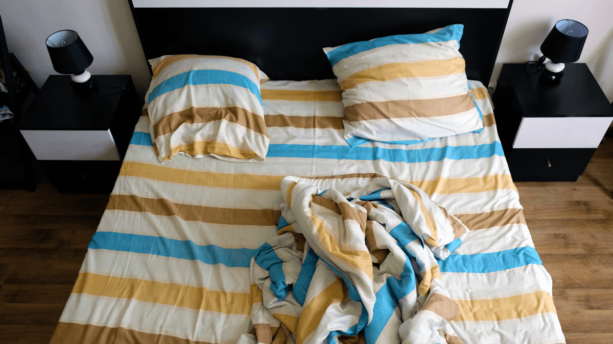 Striped bed sheets and pillows in blue, white, beige, and yellow with a matching duvet cover on a modern bed.
