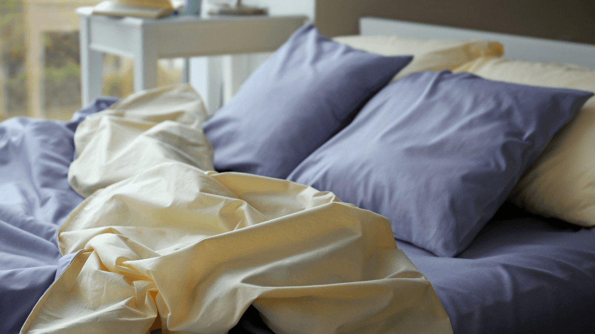 Soft blue and cream bed sheets and pillows arranged on a comfortable bedroom bed.